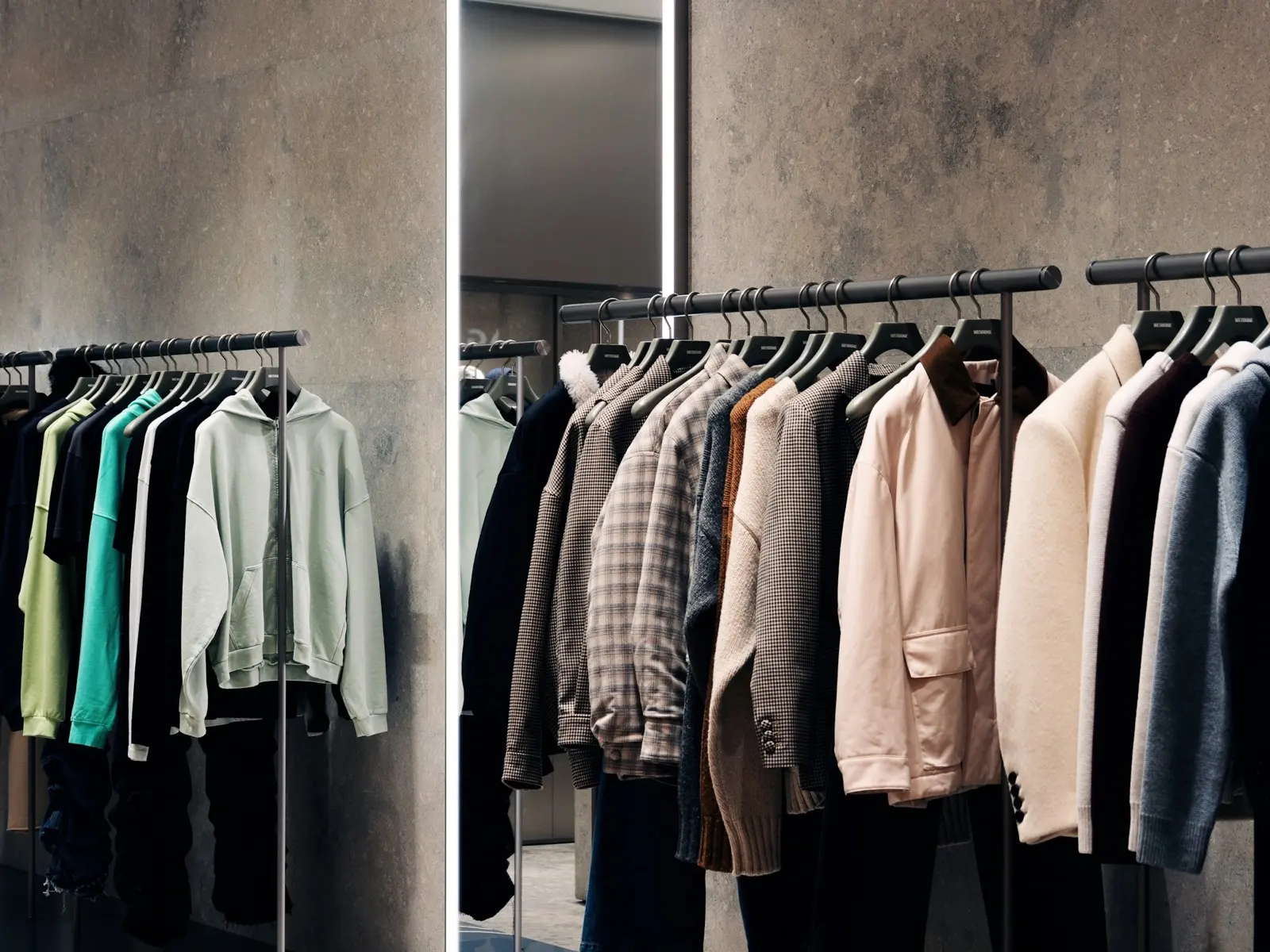 Jackets, knitwear and shirts hanging on rails in a clothing shop beside a full-length mirror