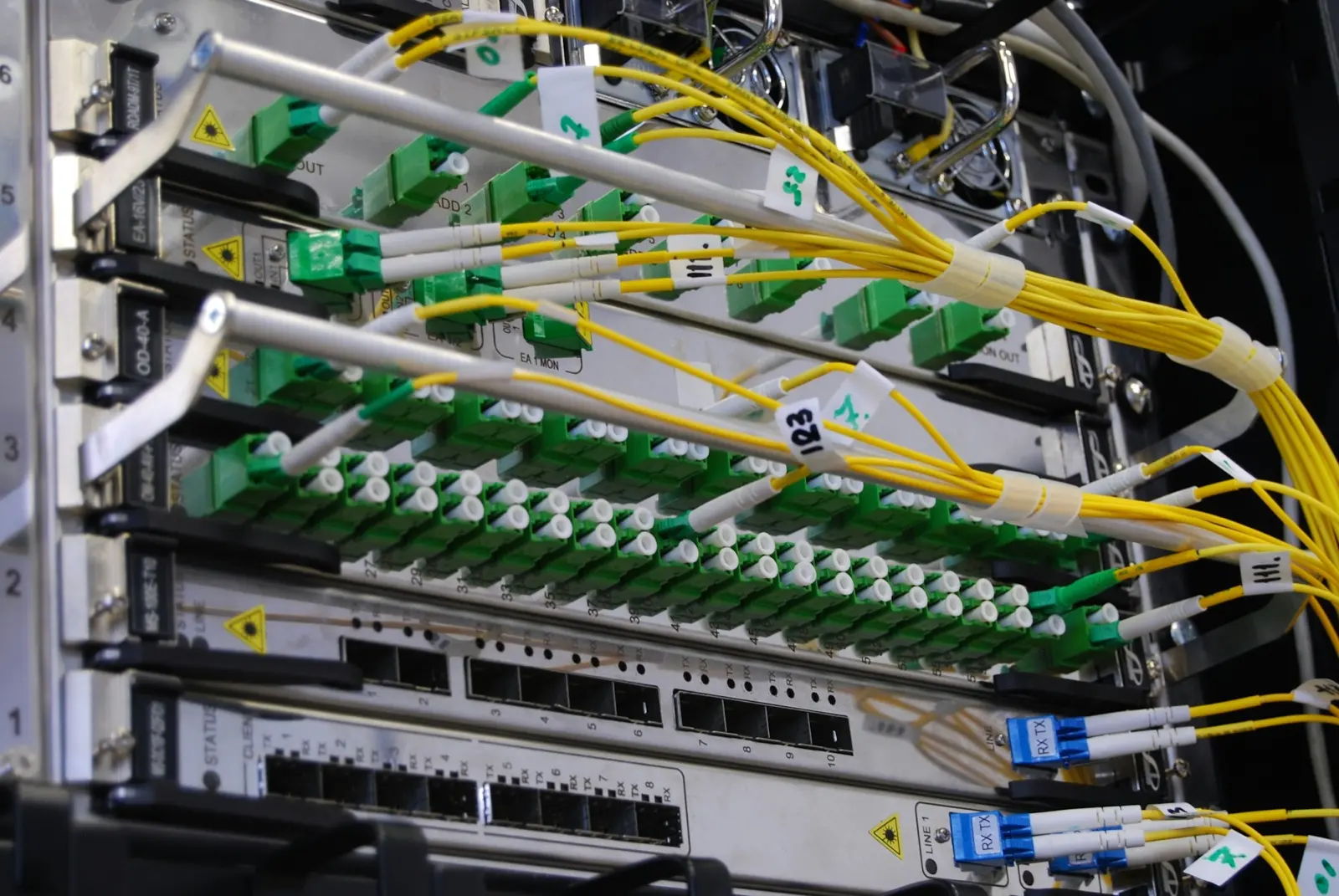 Yellow fibre optic cables plugged into green connectors on telecoms equipment in a rack