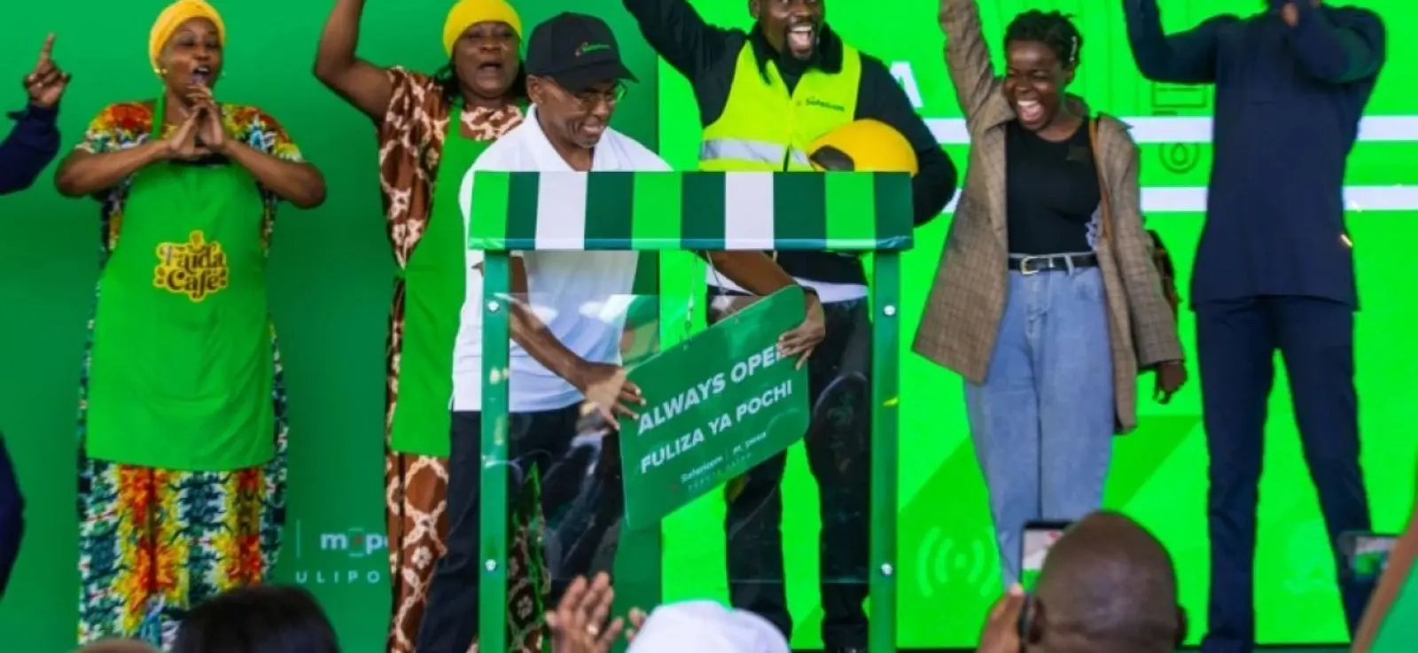 Traders and Safaricom staff cheer on stage as an Always Open Fuliza Ya Pochi sign is unveiled at the launch in Thika