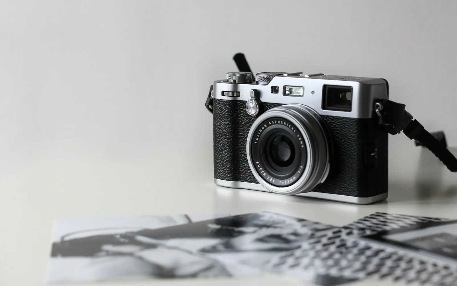 A silver and black compact camera on a white table, with black-and-white printed photographs in the foreground