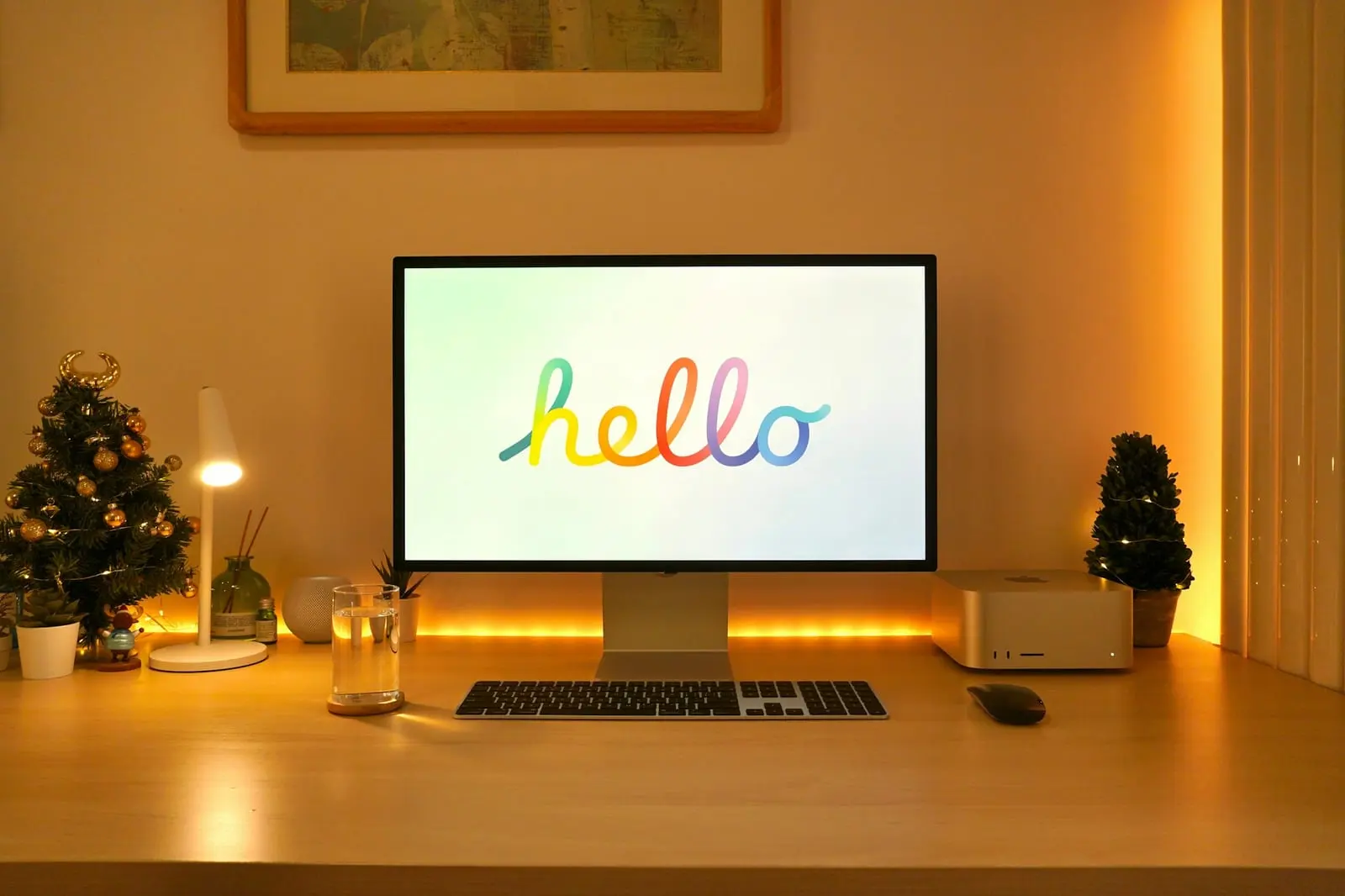 A Mac Studio and display on a wooden desk lit with warm light