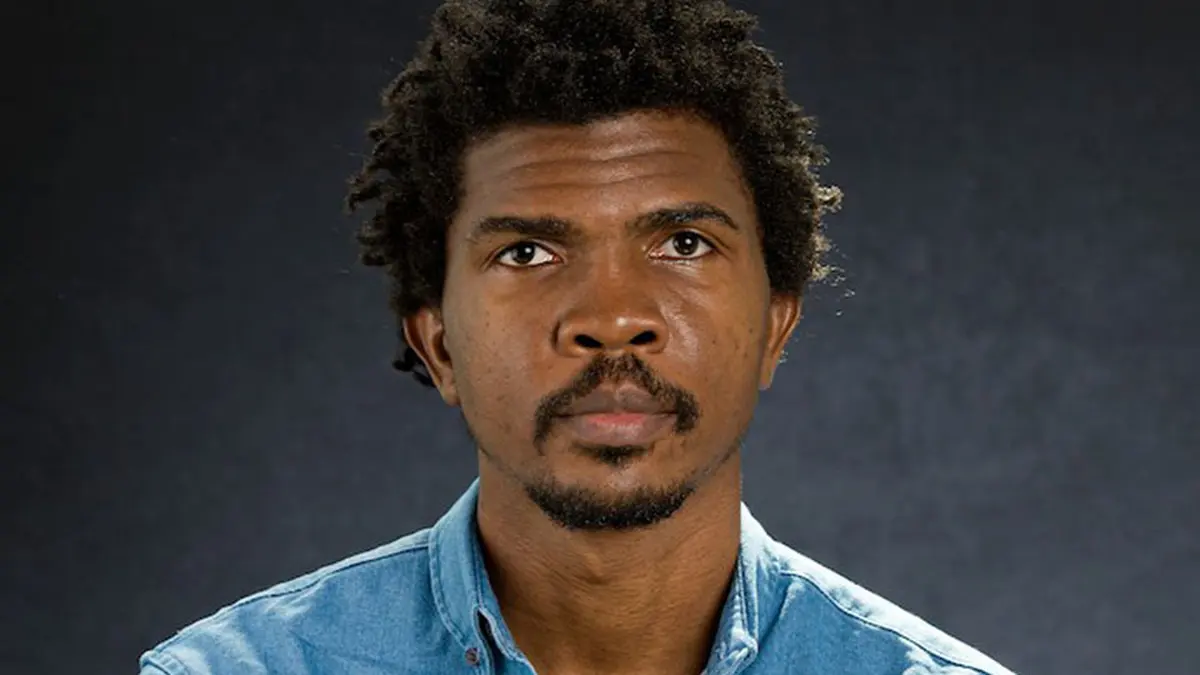 Portrait of Emmanuel Adegboye, head of Madica, in a blue denim shirt against a dark background