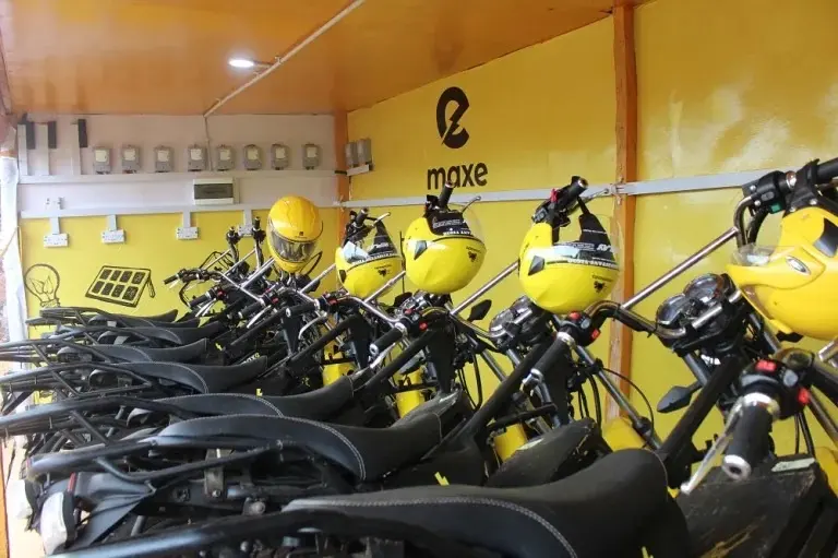 A row of electric motorcycles with yellow helmets parked inside a MAX battery and charging station