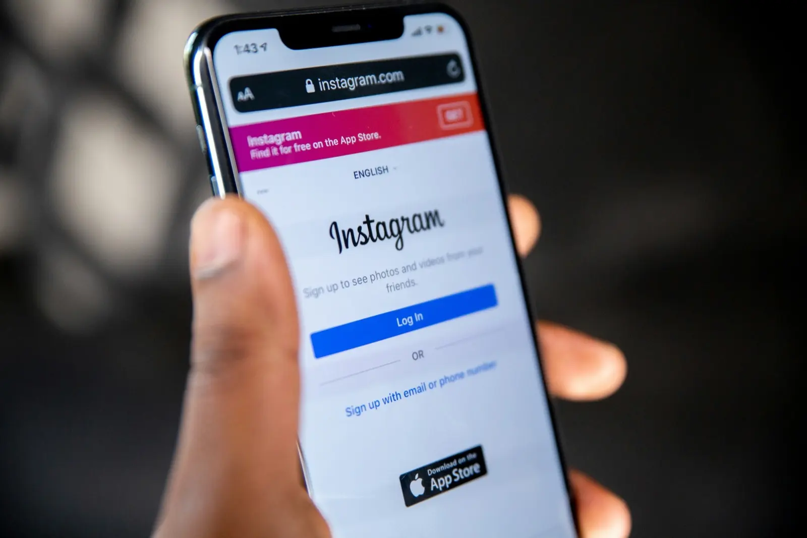 A hand holds a smartphone showing the Instagram log-in page in a web browser