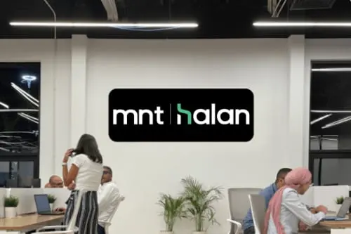 The MNT-Halan logo on a wall above people working at desks in an open office