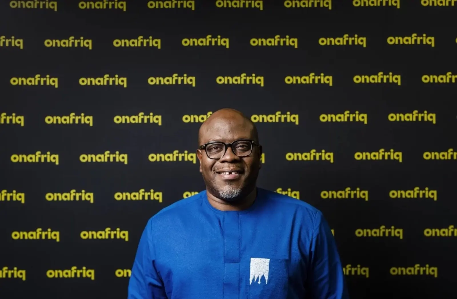 Dare Okoudjou, founder and chief executive of Onafriq, in a blue shirt in front of an Onafriq-branded wall