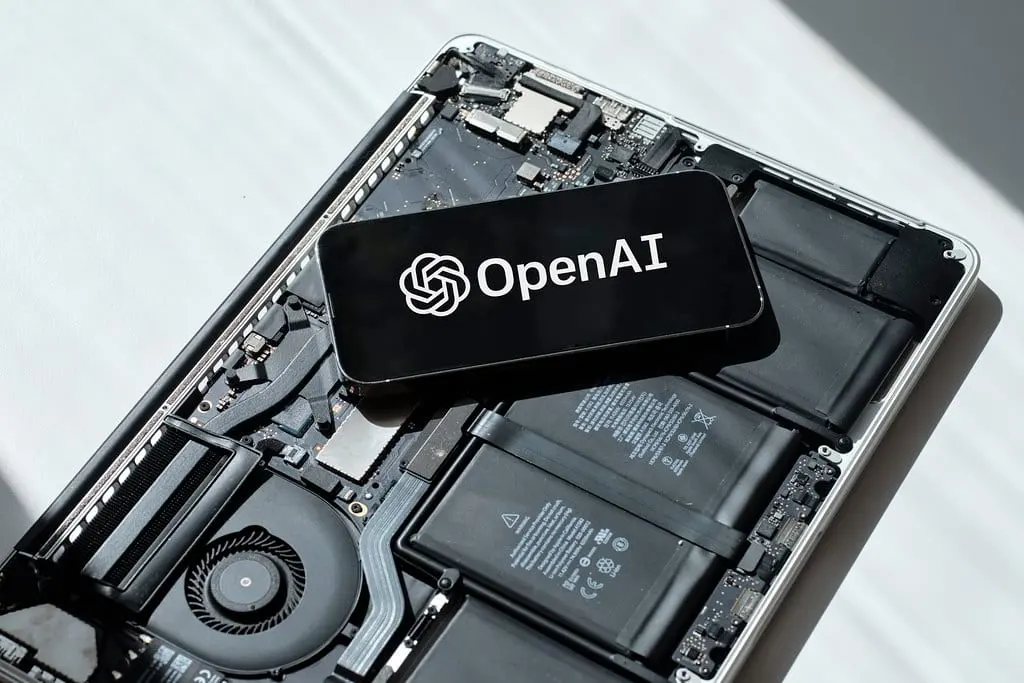 A phone showing the OpenAI logo resting on the open insides of a laptop