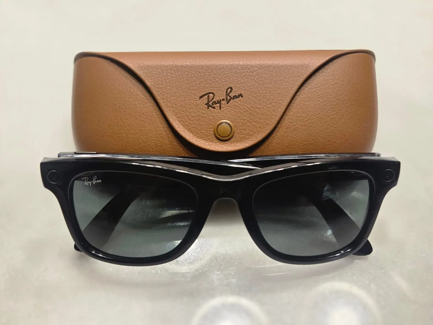 A pair of black Ray-Ban Meta smart glasses resting in front of a brown leather case