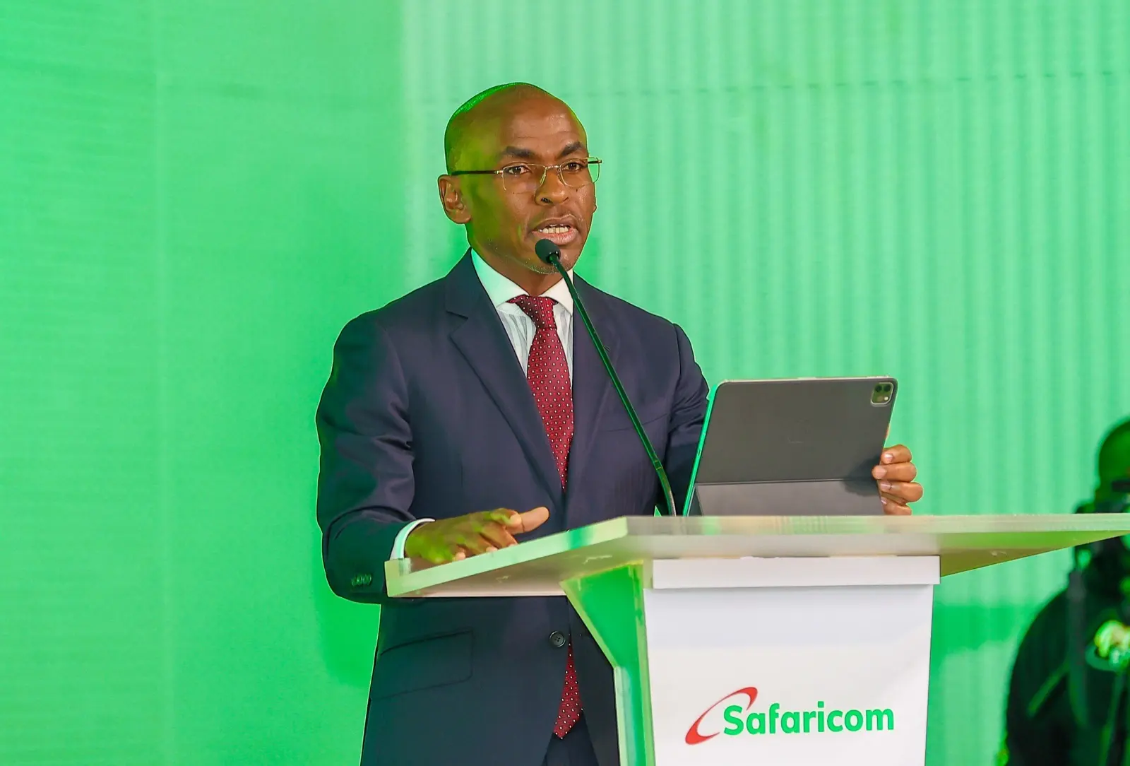 Safaricom chief executive Peter Ndegwa speaking at a Safaricom lectern against a green backdrop