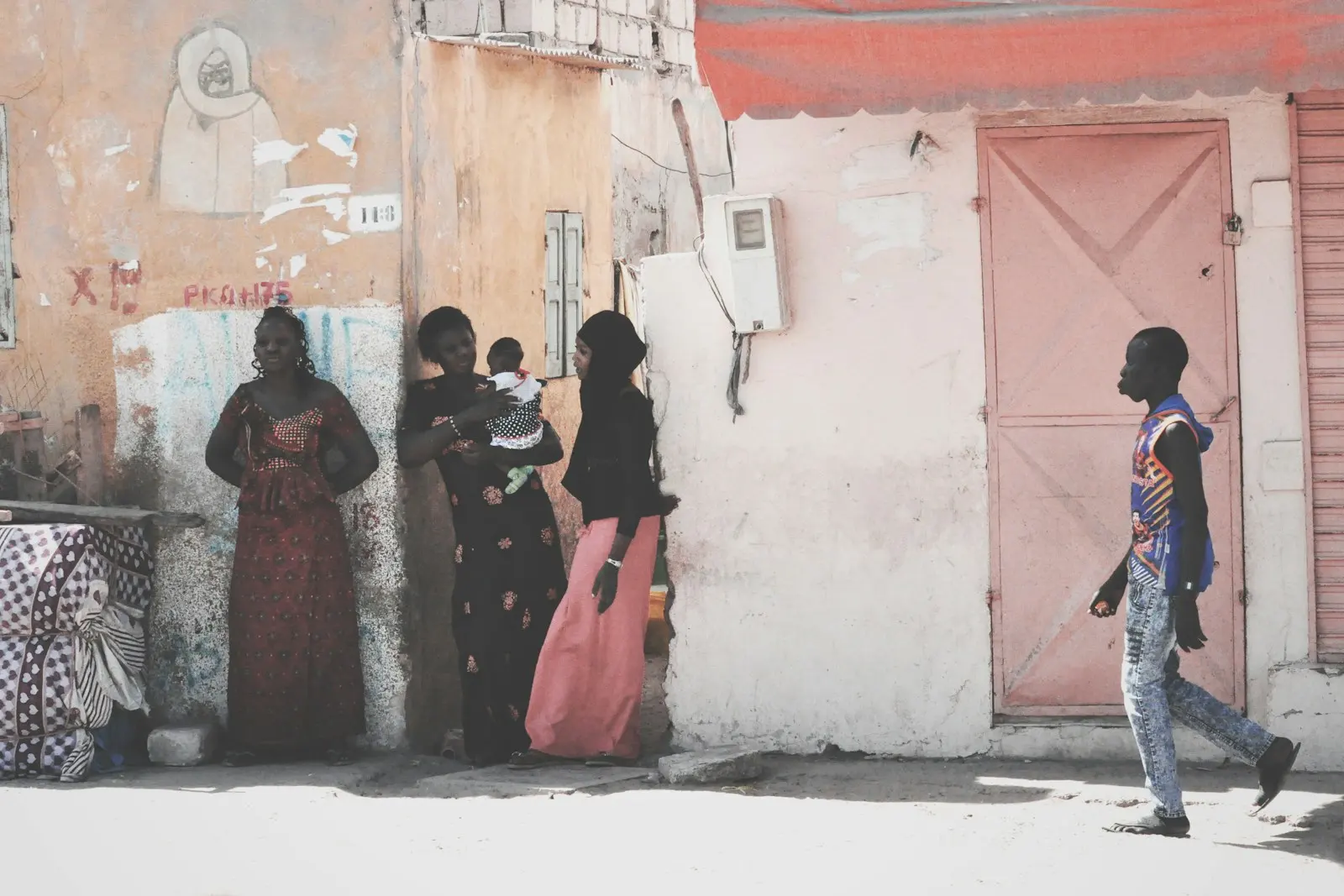 Women and a young man on a sunny street beside pastel walls in Saint-Louis, Senegal