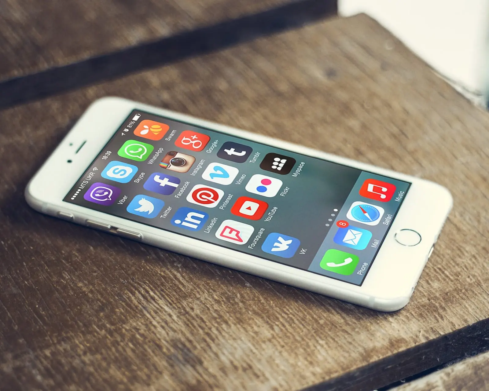 A smartphone on a wooden table showing a screen full of social media app icons