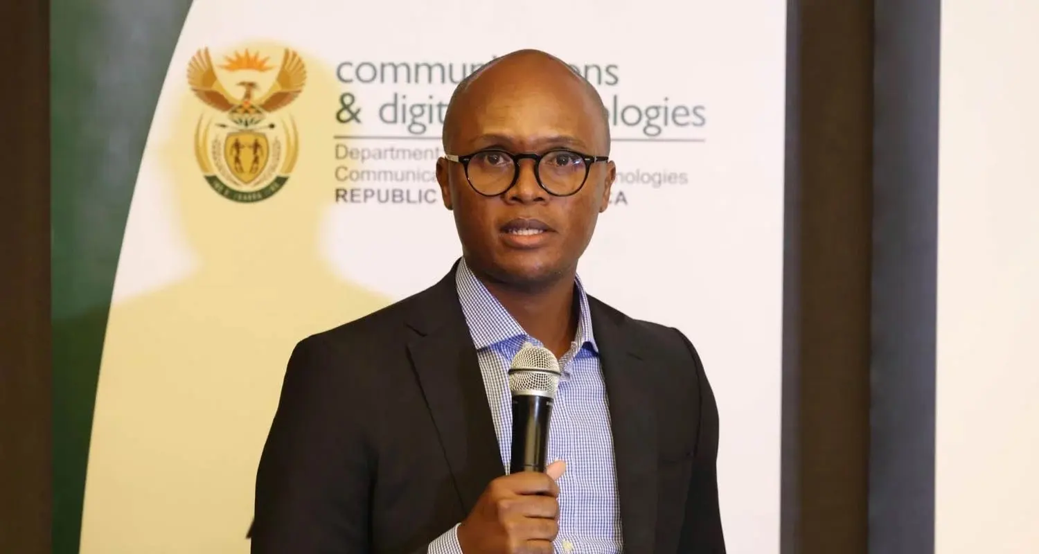 South Africa's communications minister Solly Malatsi speaking into a microphone in front of a department banner